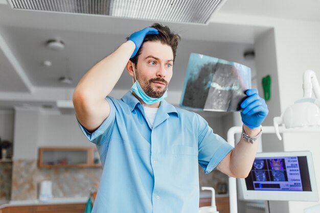 Retrato de médico o dentista con barba con rostro emocional mirando rayos x, en su oficina moderna.