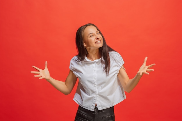 Retrato de medio cuerpo femenino hermoso aislado en fondo de estudio rojo. La joven mujer sorprendida emocional