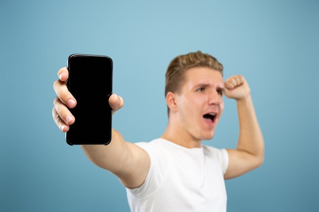 Retrato de medio cuerpo del joven caucásico en estudio azul