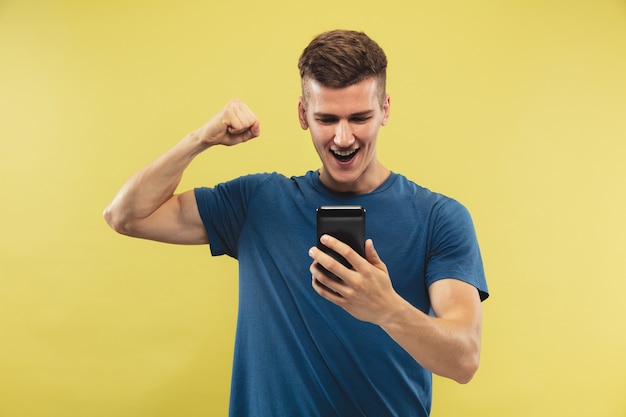 Retrato de medio cuerpo del joven caucásico sobre fondo amarillo de estudio. Hermoso modelo masculino en camisa azul. Concepto de emociones humanas, expresión facial. Apuestas deportivas, compras online, venta.