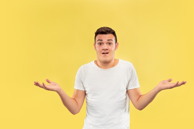 Retrato de medio cuerpo del joven caucásico sobre fondo amarillo de estudio. Hermoso modelo masculino en camisa. Concepto de emociones humanas, expresión facial, ventas, publicidad. Mostrando algo, parece incierto.