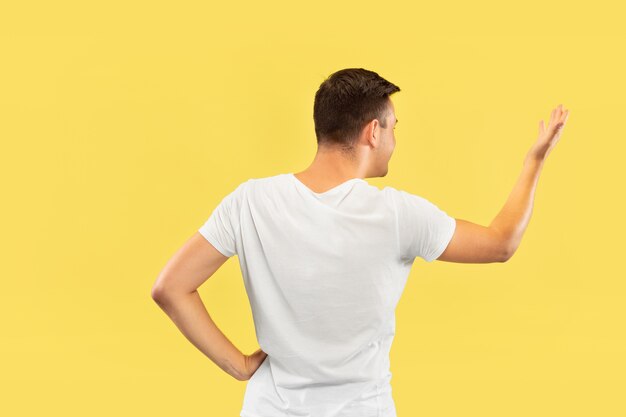 Retrato de medio cuerpo del joven caucásico sobre fondo amarillo de estudio. Hermoso modelo masculino en camisa. Concepto de emociones humanas, expresión facial, ventas, publicidad. Mostrando y señalando algo.