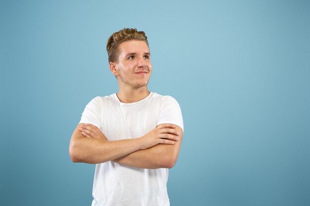 Retrato de medio cuerpo del joven caucásico sobre fondo azul de estudio. Hermoso modelo masculino en camisa. Concepto de emociones humanas, expresión facial, ventas, publicidad. De pie y sonriendo, parece confiado.