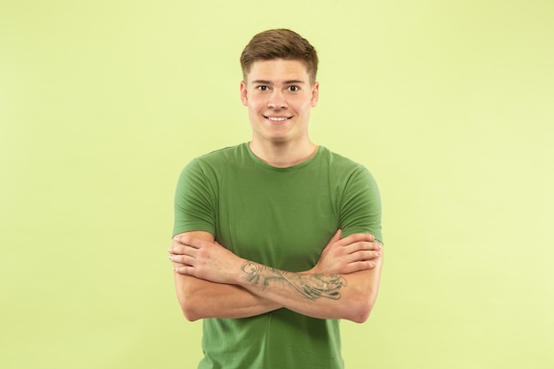 Foto gratuita retrato de medio cuerpo del joven caucásico sobre fondo verde de estudio. hermoso modelo masculino en camisa. concepto de emociones humanas, expresión facial, ventas, publicidad. de pie con las manos cruzadas, sonriendo.