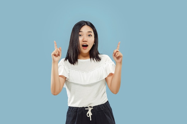 Retrato de medio cuerpo de la joven coreana. Modelo femenino en camisa blanca. Mostrando y señalando algo. Concepto de emociones humanas, expresión facial. Vista frontal.