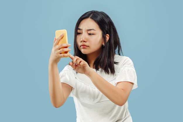 Retrato de medio cuerpo de la joven coreana. Modelo femenino en camisa blanca. Usando su teléfono inteligente. Concepto de emociones humanas, expresión facial. Vista frontal.