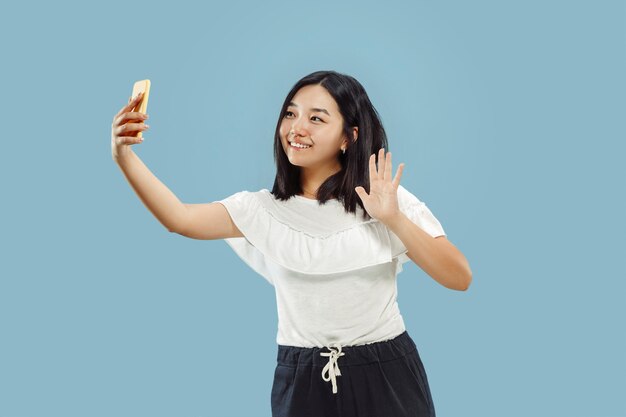 Retrato de medio cuerpo de la joven coreana sobre fondo azul.