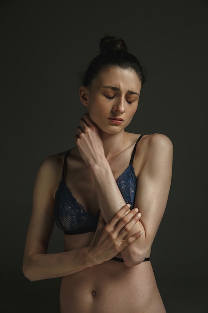 Retrato de medio cuerpo de una joven mujer triste en ropa interior en la pared oscura. Tristeza, depresión y adicción. Concepto de emociones humanas, feminismo, problemas y derechos de la mujer, salud mental.