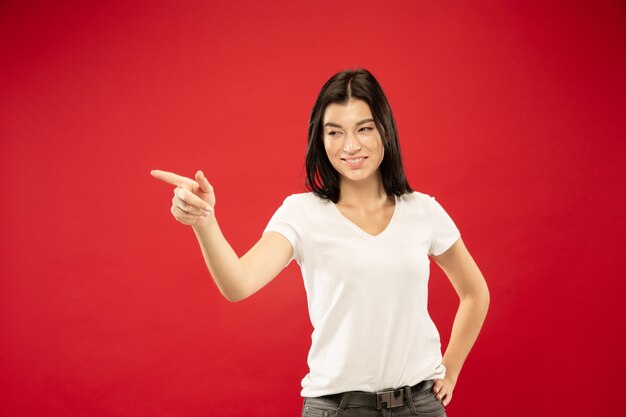 Retrato de medio cuerpo de la mujer joven caucásica en estudio rojo