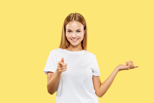 Retrato de medio cuerpo de la mujer joven caucásica sobre fondo amarillo de estudio. Modelo de mujer hermosa en camisa blanca. Concepto de emociones humanas, expresión facial. Mostrando y señalando algo.