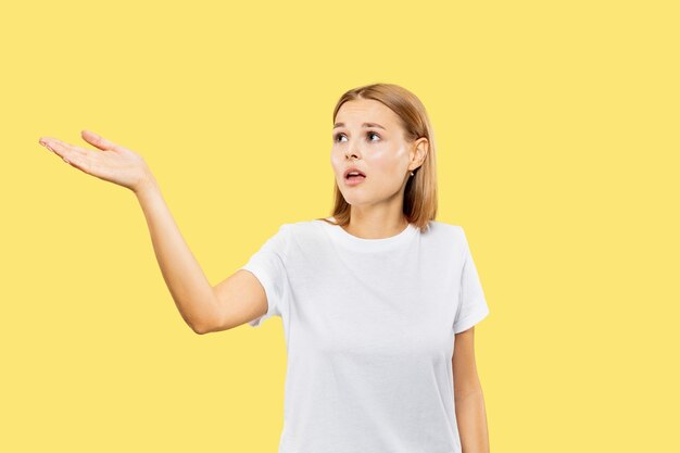 Retrato de medio cuerpo de la mujer joven caucásica sobre fondo amarillo de estudio. Modelo de mujer hermosa en camisa blanca. Concepto de emociones humanas, expresión facial. Mostrar un espacio vacío o invitar.