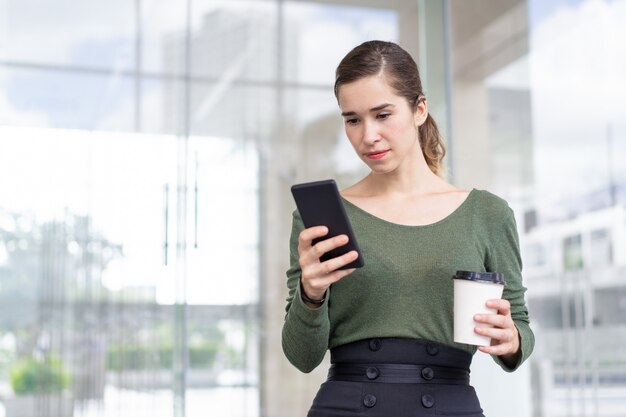 Retrato del mensaje concentrado de la lectura de la mujer joven en el teléfono