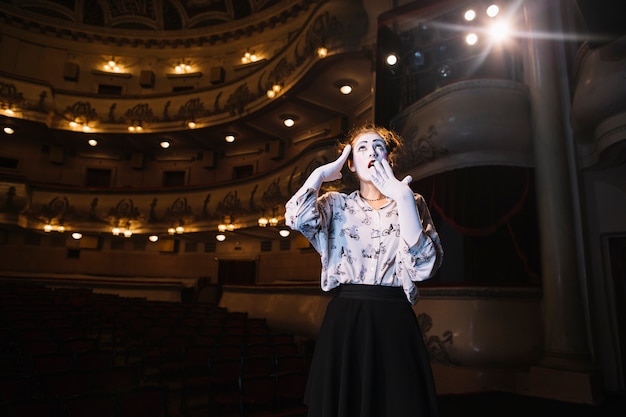 Retrato de mime femenino sorprendido de pie en el auditorio mirando hacia arriba