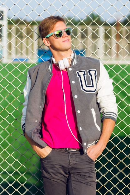 Retrato de moda al aire libre de chico guapo en elegante traje deportivo de primavera y posando cerca del campo de deportes.