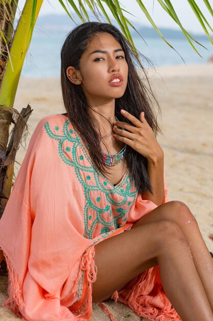 Retrato de moda al aire libre de mujer asiática en playa tropical, ella se está relajando, soñando. Llevando joyas, brazalete y collar.