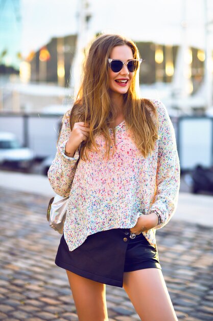 Retrato de moda al aire libre de mujer bonita rubia caminando sola en un agradable día soleado de otoño, acogedora minifalda swather, luz del sol de la tarde.