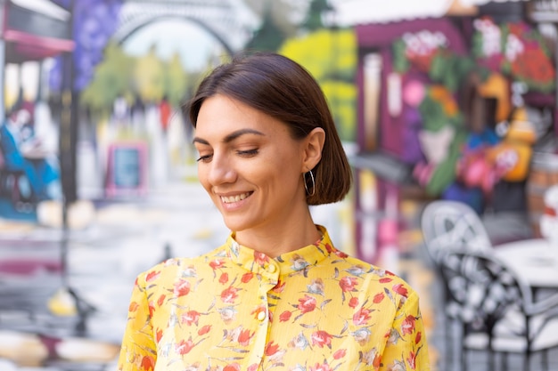 Retrato de moda al aire libre de mujer en vestido amarillo de verano en la pared colorida de la calle