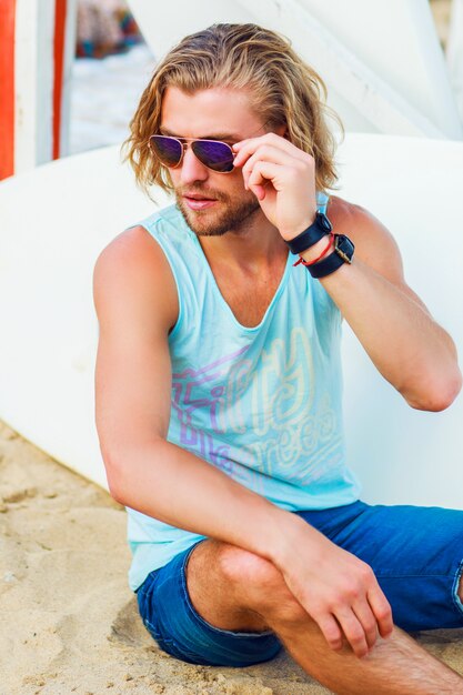 Retrato de moda de un atractivo joven sexy con cabello largo y claro perfecto en una playa tropical