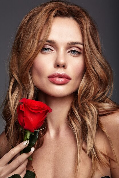 Retrato de moda de belleza de joven rubia modelo con maquillaje natural y piel perfecta con hermosa rosa posando