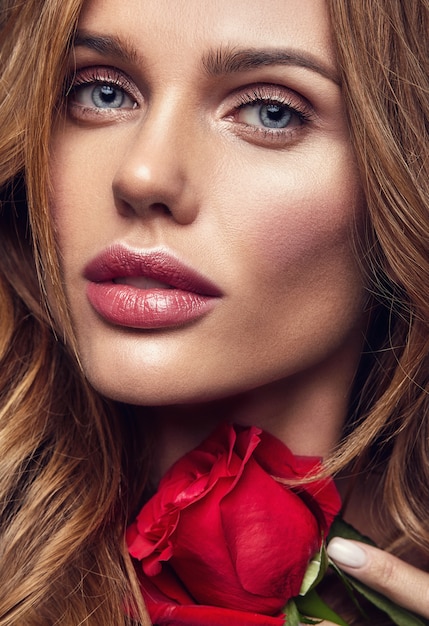 Retrato de moda de belleza de joven rubia modelo con maquillaje natural y piel perfecta con hermosa rosa posando