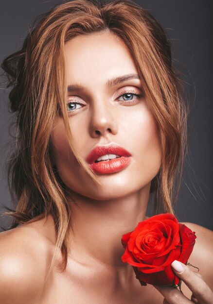 Retrato de moda de belleza de joven rubia modelo con maquillaje natural y piel perfecta con hermosa rosa posando