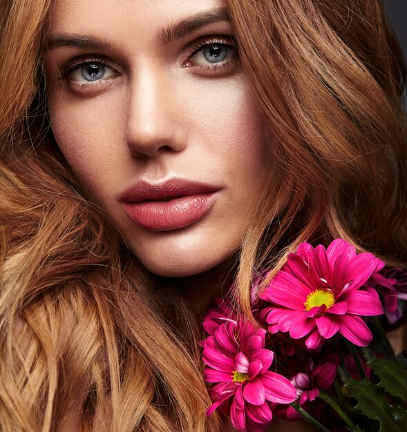 Retrato de moda de belleza de modelo de mujer joven rubia con maquillaje natural y piel perfecta con brillante flor de crisantemo rimson posando