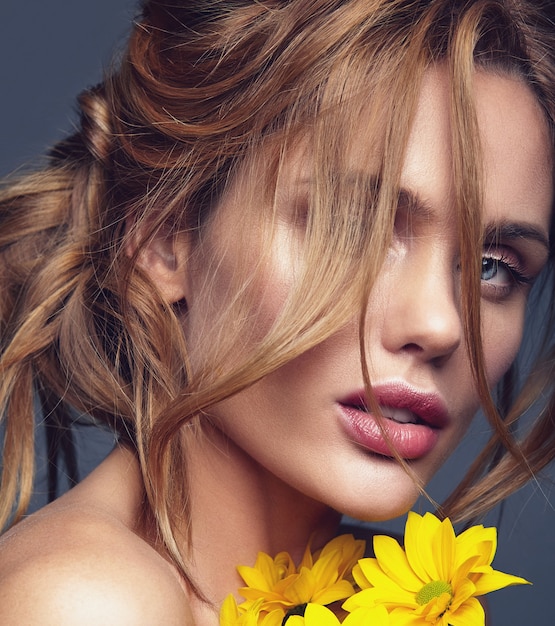 Retrato de moda de belleza de mujer joven rubia modelo con maquillaje natural y piel perfecta con flor de crisantemo amarillo brillante posando