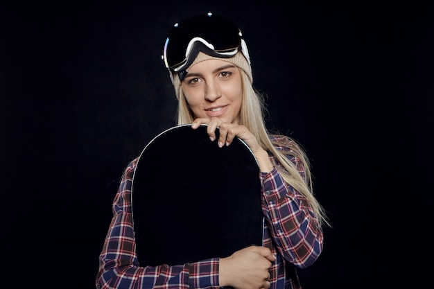 Foto gratuita retrato de moda chica rubia con gafas protectoras y camisa a cuadros sosteniendo snowboard negro