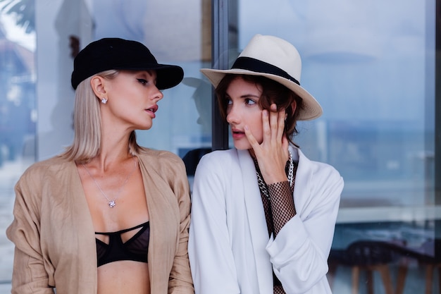 Retrato de moda de dos elegantes mujeres caucásicas en blazers gorra francesa y soporte de sombrero blanco clásico