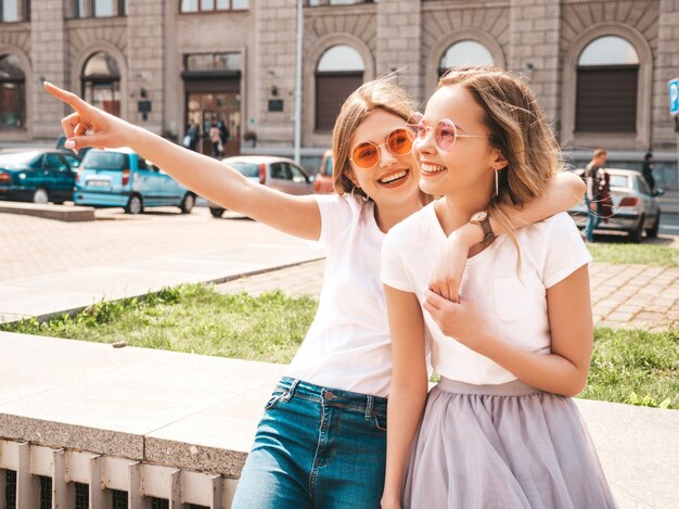 Retrato de moda de dos jóvenes hippie con estilo morena y rubia mujeres modelos en día soleado de verano en ropa hipster blanco posando