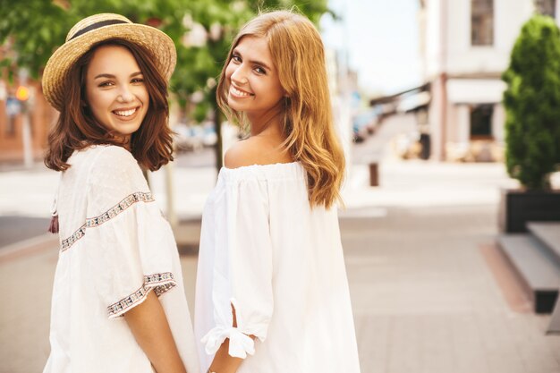 Retrato de moda de dos jóvenes hippie con estilo morena y rubia mujeres modelos sin maquillaje en día soleado de verano en ropa hipster blanco posando. Giro de vuelta