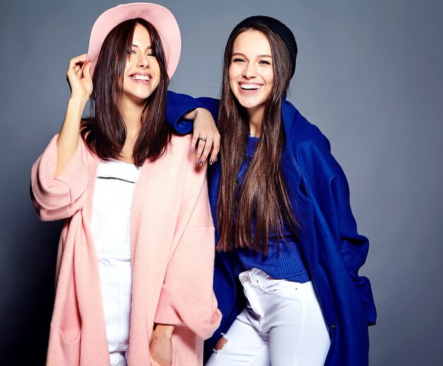 Retrato de moda de dos modelos de mujeres morenas sonrientes en verano casual hipster abrigo posando en gris