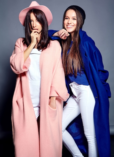 Retrato de moda de dos modelos de mujeres morenas sonrientes en verano casual hipster abrigo posando en gris