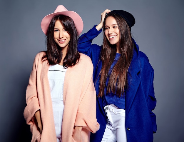 Retrato de moda de dos modelos de mujeres morenas sonrientes en verano casual hipster abrigo posando en gris