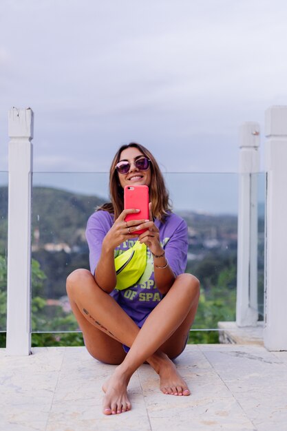 Retrato de moda con estilo europeo joven en forma bronceada mujer en vestido de camisa larga púrpura gafas de sol