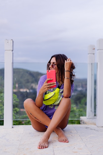 Retrato de moda con estilo europeo joven en forma bronceada mujer en vestido de camisa larga púrpura gafas de sol