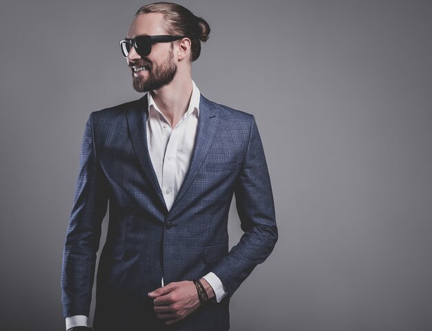 Retrato de moda guapo elegante hipster empresario modelo vestido con elegante traje azul con gafas de sol posando en gris