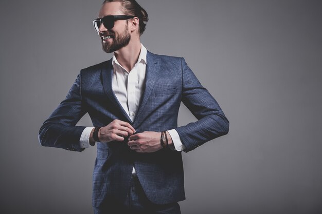 Retrato de moda guapo elegante hipster empresario modelo vestido con elegante traje azul con gafas de sol posando en gris