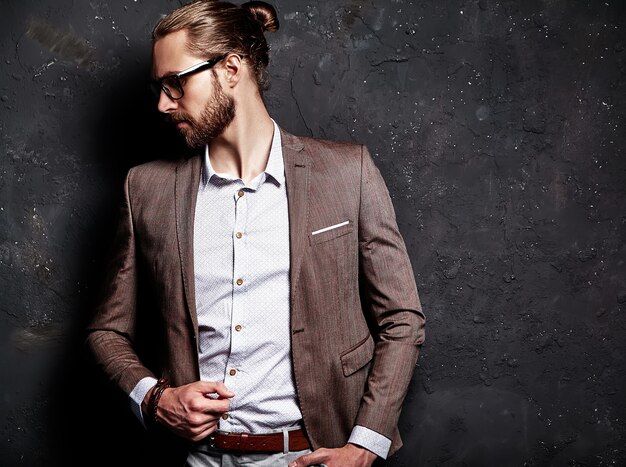 Retrato de moda guapo elegante hipster empresario modelo vestido con elegante traje marrón con gafas cerca de la pared oscura