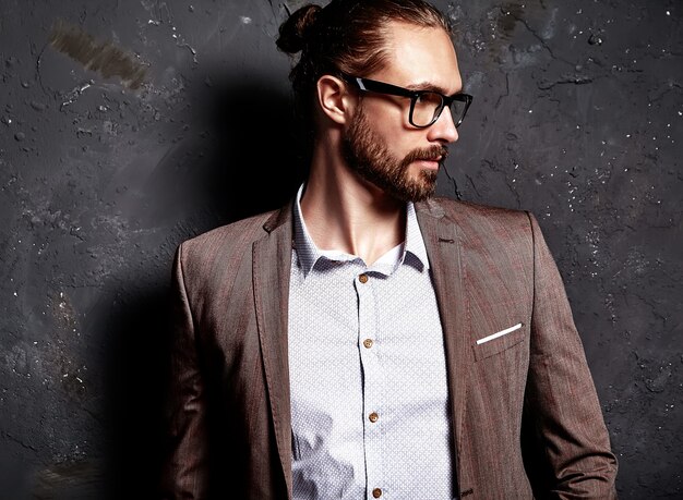 Retrato de moda guapo elegante hipster empresario modelo vestido con elegante traje marrón con gafas cerca de la pared oscura