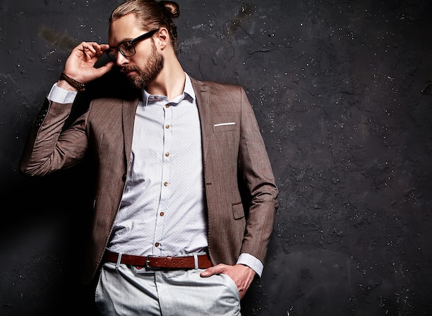 Retrato de moda guapo elegante hipster empresario modelo vestido con elegante traje marrón con gafas cerca de la pared oscura