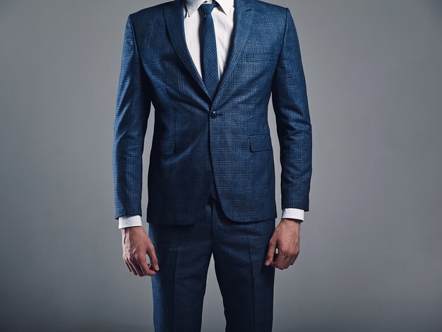Retrato de moda guapo empresario elegante modelo vestido con elegante traje azul posando sobre fondo gris en estudio
