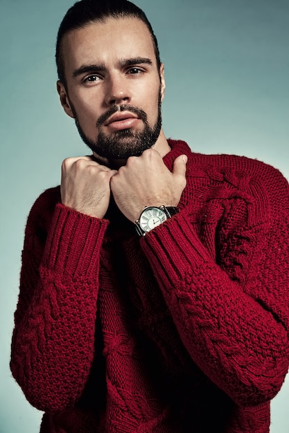 Retrato de moda guapo modelo hipster elegante vestido con suéter rojo cálido posando en el estudio.