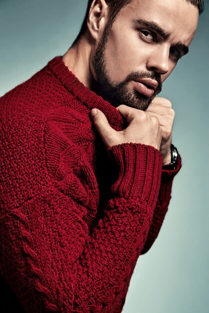 Retrato de moda guapo modelo hipster elegante vestido con suéter rojo cálido posando en el estudio.