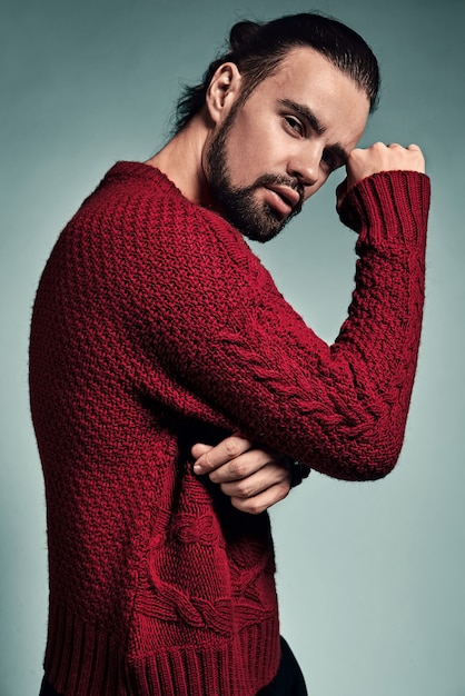 Retrato de moda guapo modelo hipster elegante vestido con suéter rojo cálido posando en el estudio.