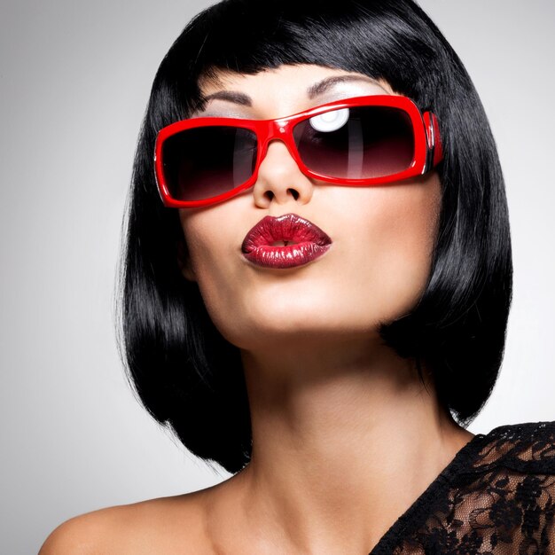 Retrato de moda de una hermosa mujer morena con peinado de tiro con gafas de sol rojas