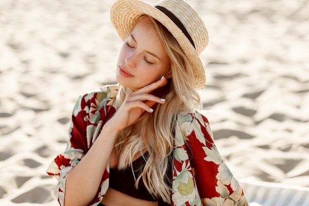 Retrato de moda de hermosa mujer rubia con maquillaje natural descansando en la playa soleada. Llevaba sombrero de paja. Vacaciones y humor de vacaciones.