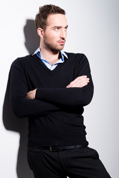 Retrato de moda de hombre joven en jersey negro y camisa azul con brazos cruzados