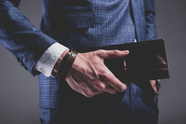 Retrato de moda de joven empresario guapo modelo hombre vestido con elegante traje azul sobre gris.