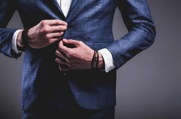 Retrato de moda de joven empresario guapo modelo hombre vestido con elegante traje azul sobre gris.